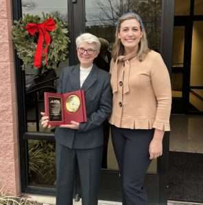 Picture of 2 women, one with gray hair holding a plaque and the other younger with her arm around the older one